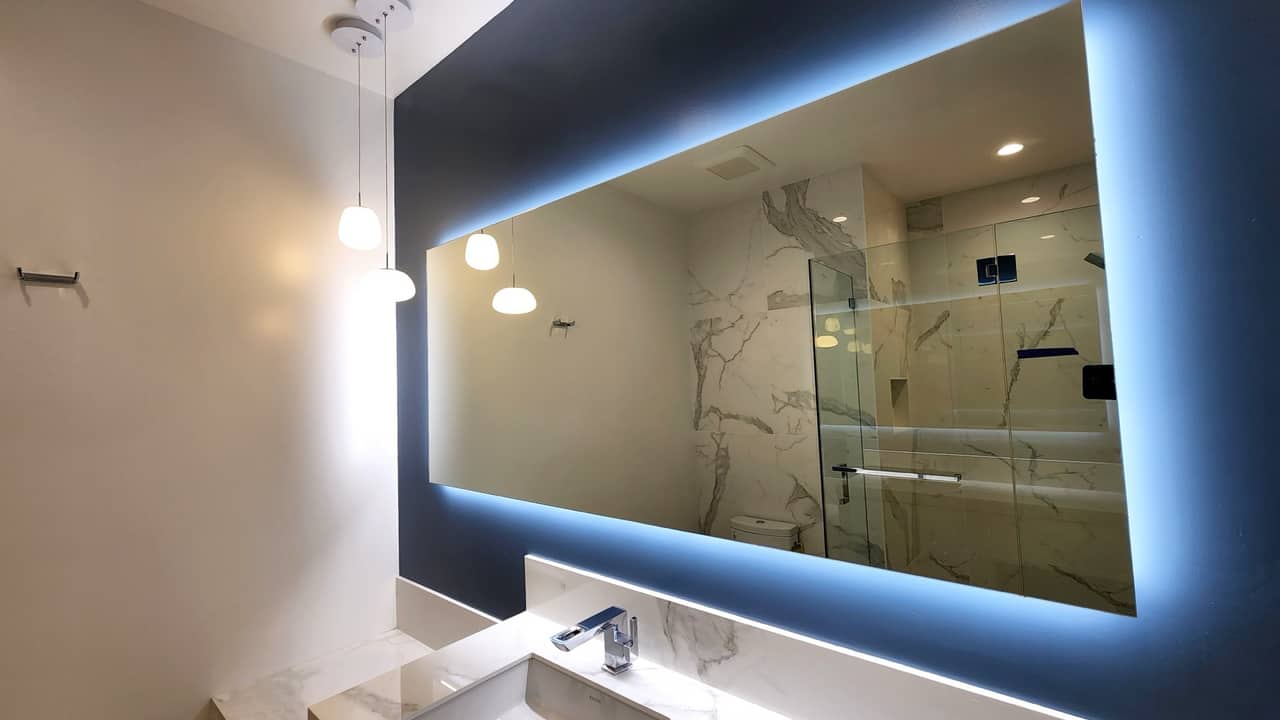 Backlit LED mirror over a floating vanity, veined marble bathroom
