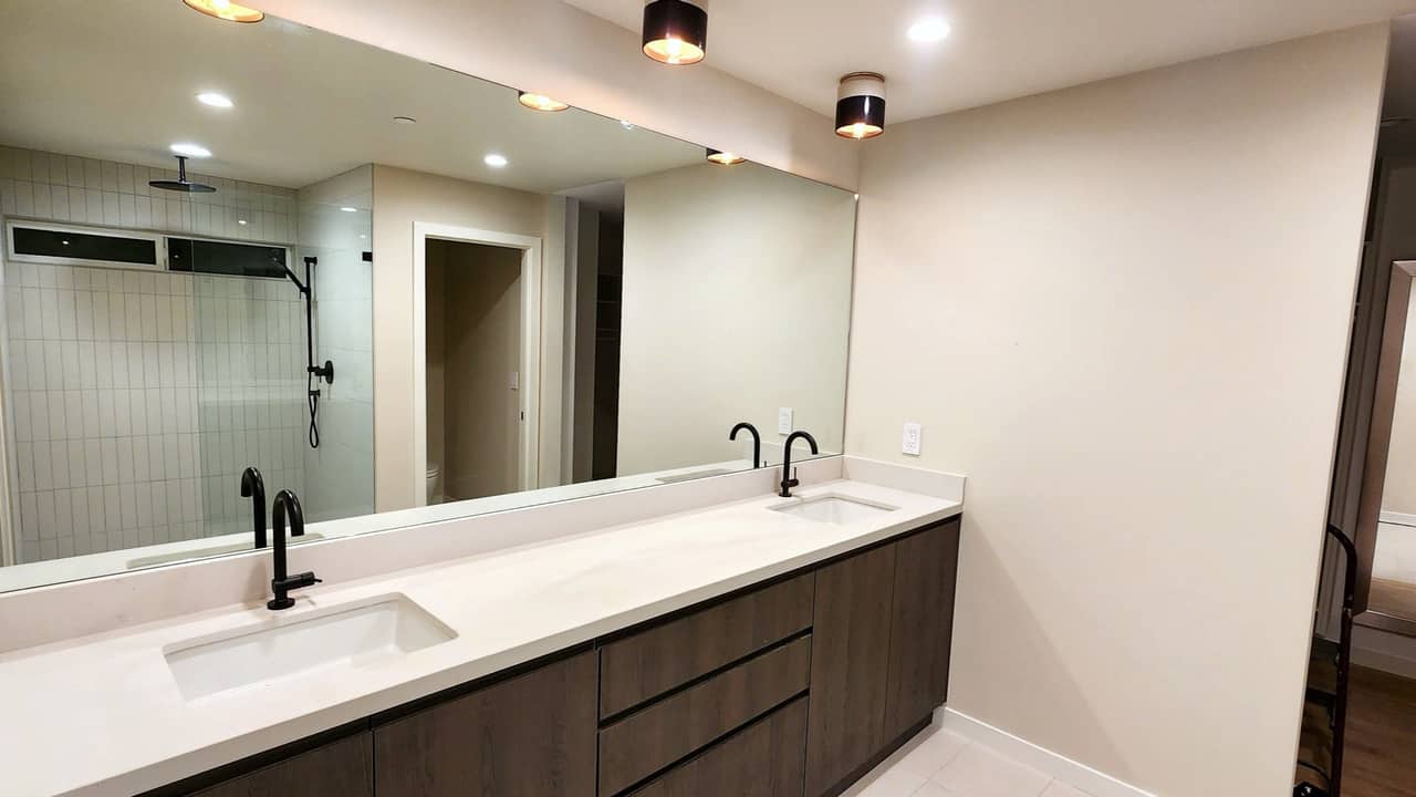Frameless wall mirror above a double vanity reflecting a walk-in shower