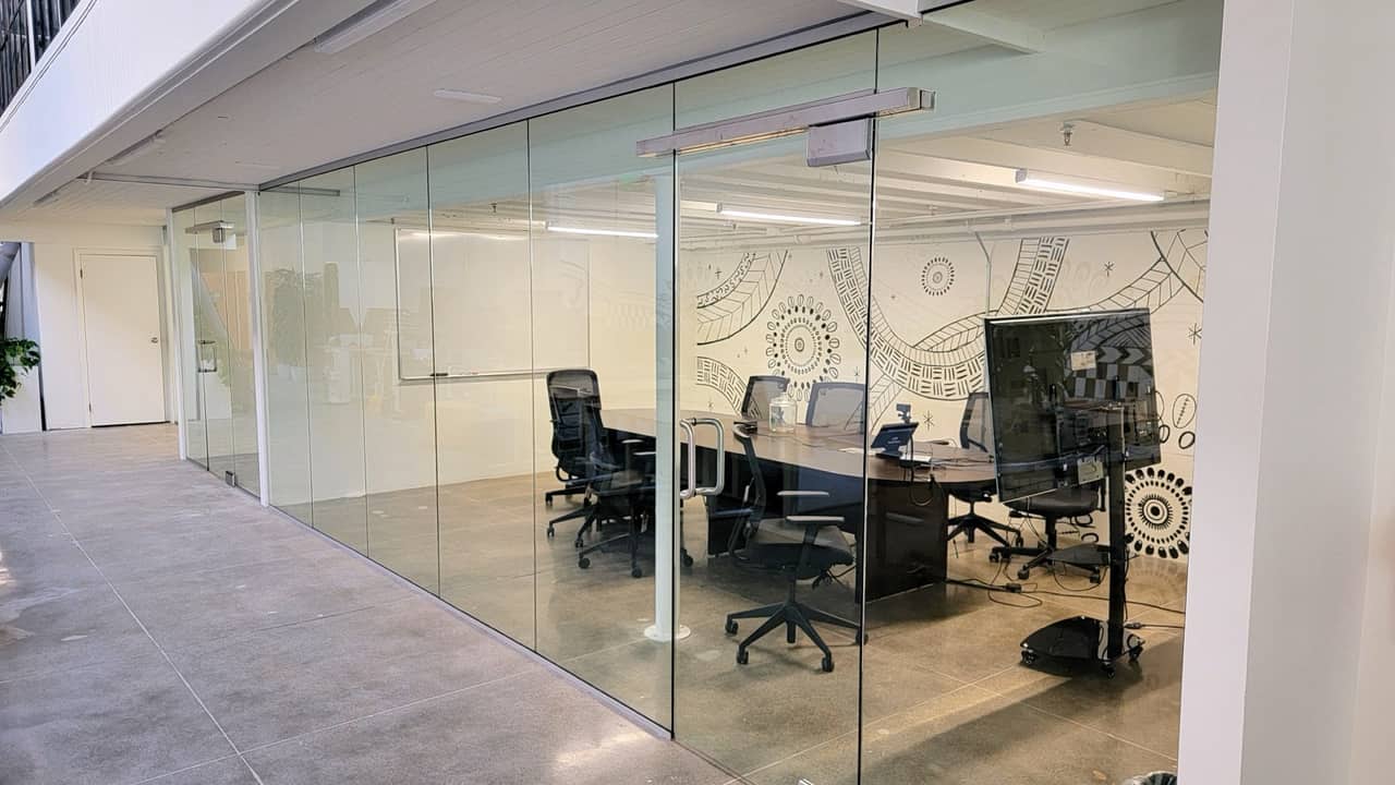 Frameless glass meeting room with a patterned mural wall on polished concrete, Bay Area