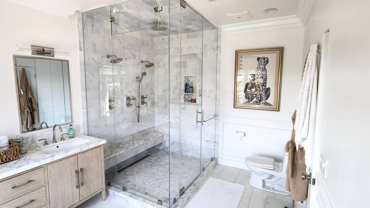 Frameless glass corner shower in carrara marble with a bench and framed cheetah print, Bay Area bath